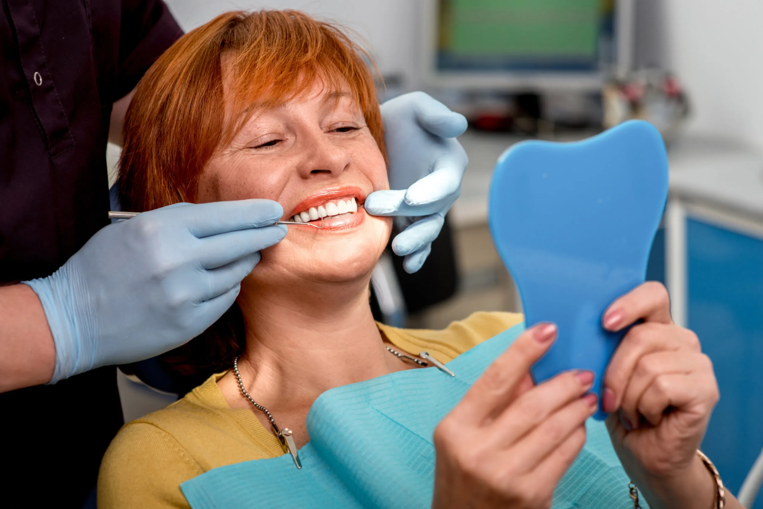 dentist in blue gloves showing a older female patient her new dental bridge